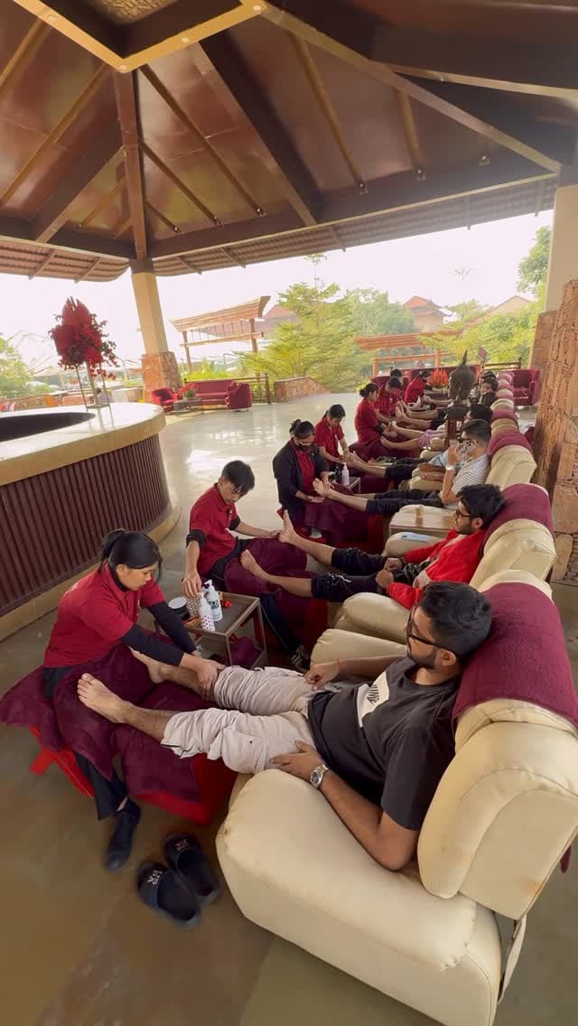 Guests receiving foot massages side by side under a covered outdoor pavilion, therapists in red uniforms seated at their feet