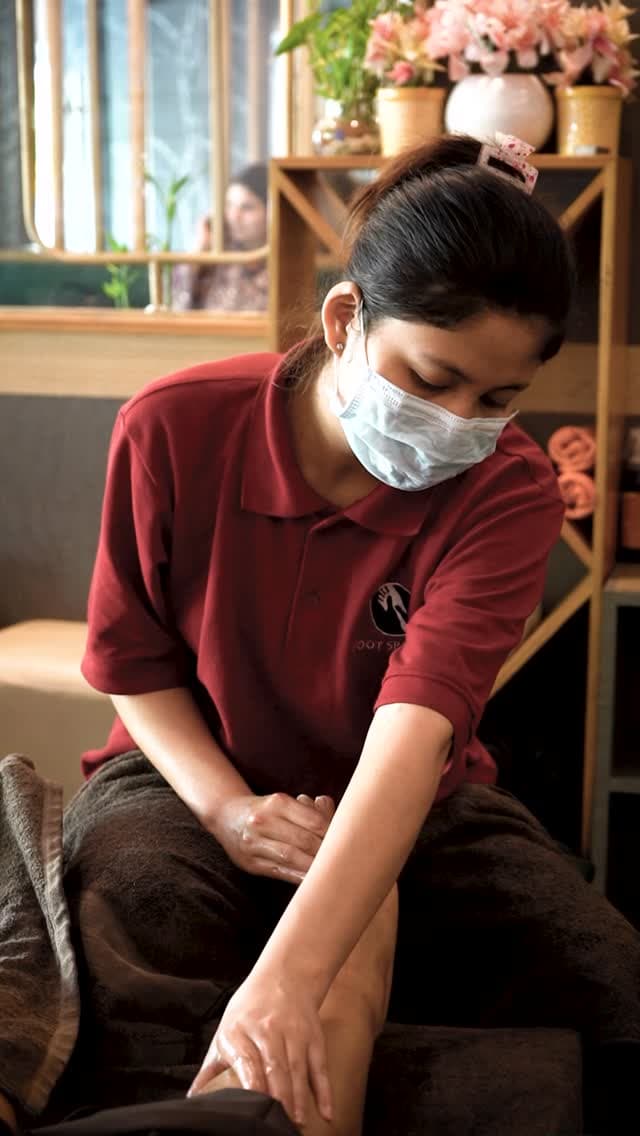 A therapist in the studio’s red uniform working on a guest’s foot, seated on a low stool